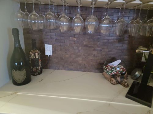 Metallic tile backsplash behind a hanging wine rack. 